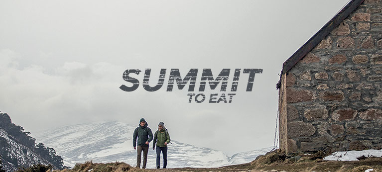 Summit To Eat logo with foggy scene with mountain hut and two walkers in background