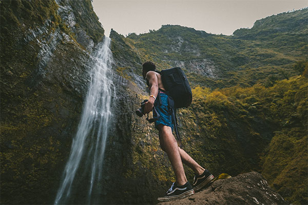a man carrying a camera by a waterfall
