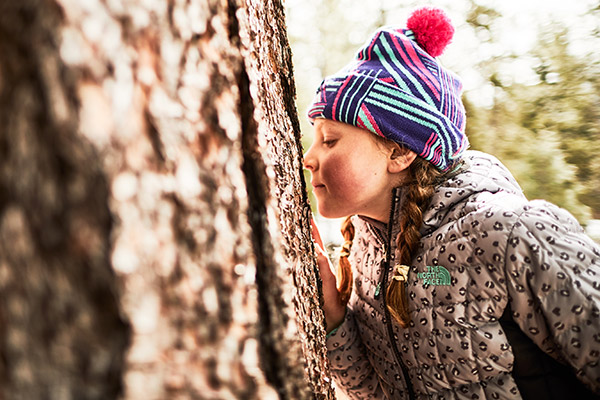 Girl in a thermoball hoodie sniffing a tree