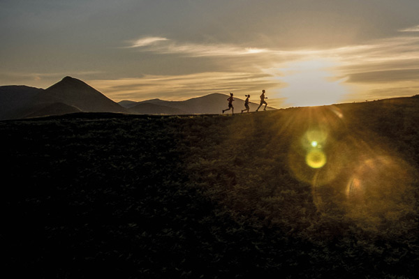 silhouette of three people running over hillside